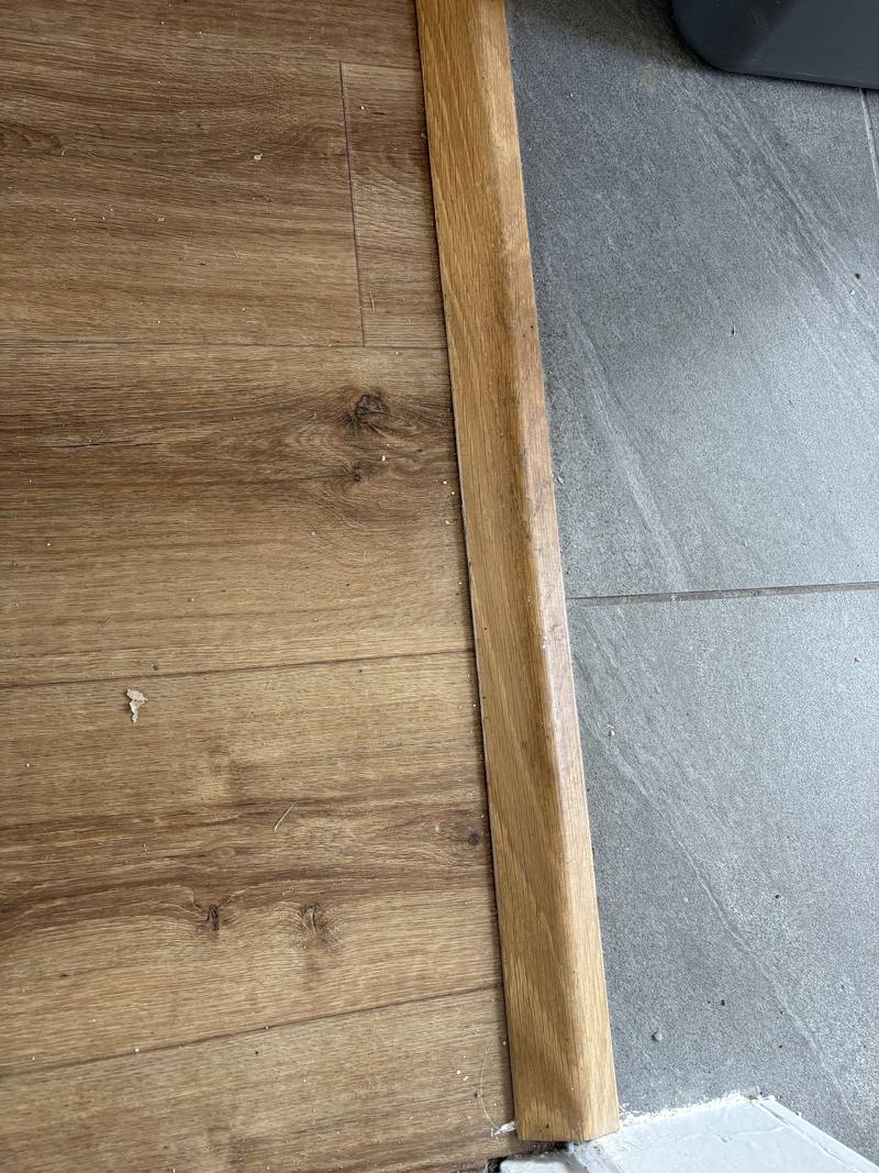 Oak threshold strip fitted between wood-effect flooring and grey floor tiles