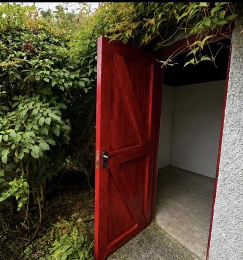 Timber ledged and braced door finished in red, hung in a garden doorway