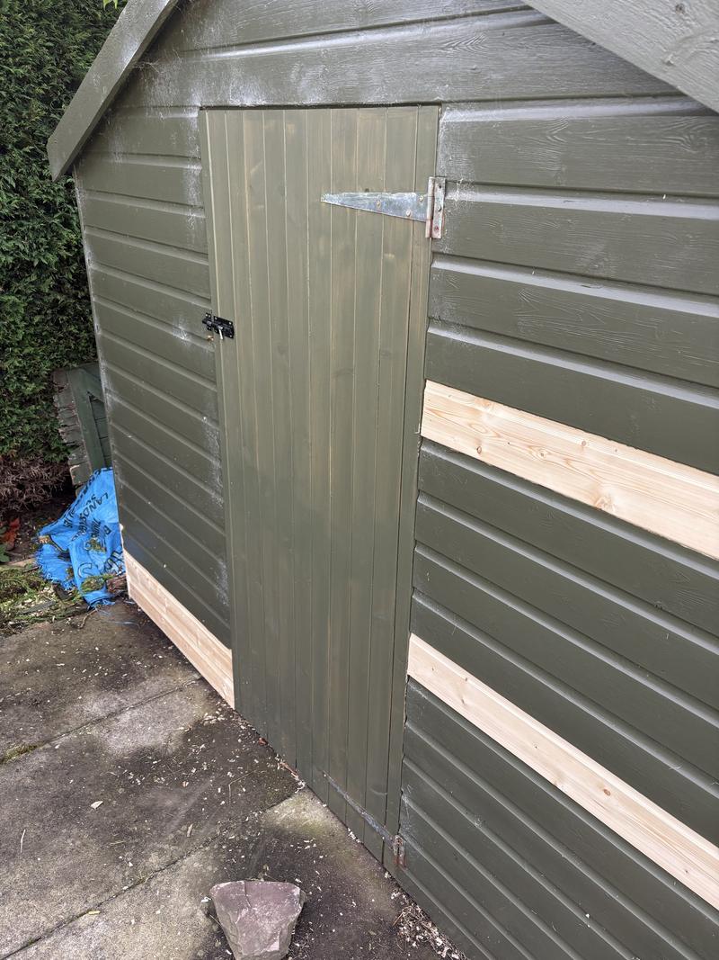 Shed with a new ledged and braced timber door fitted, and new cladding boards let into the painted wall